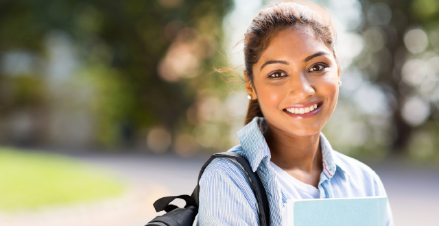 Young female student holding books outside and smiling